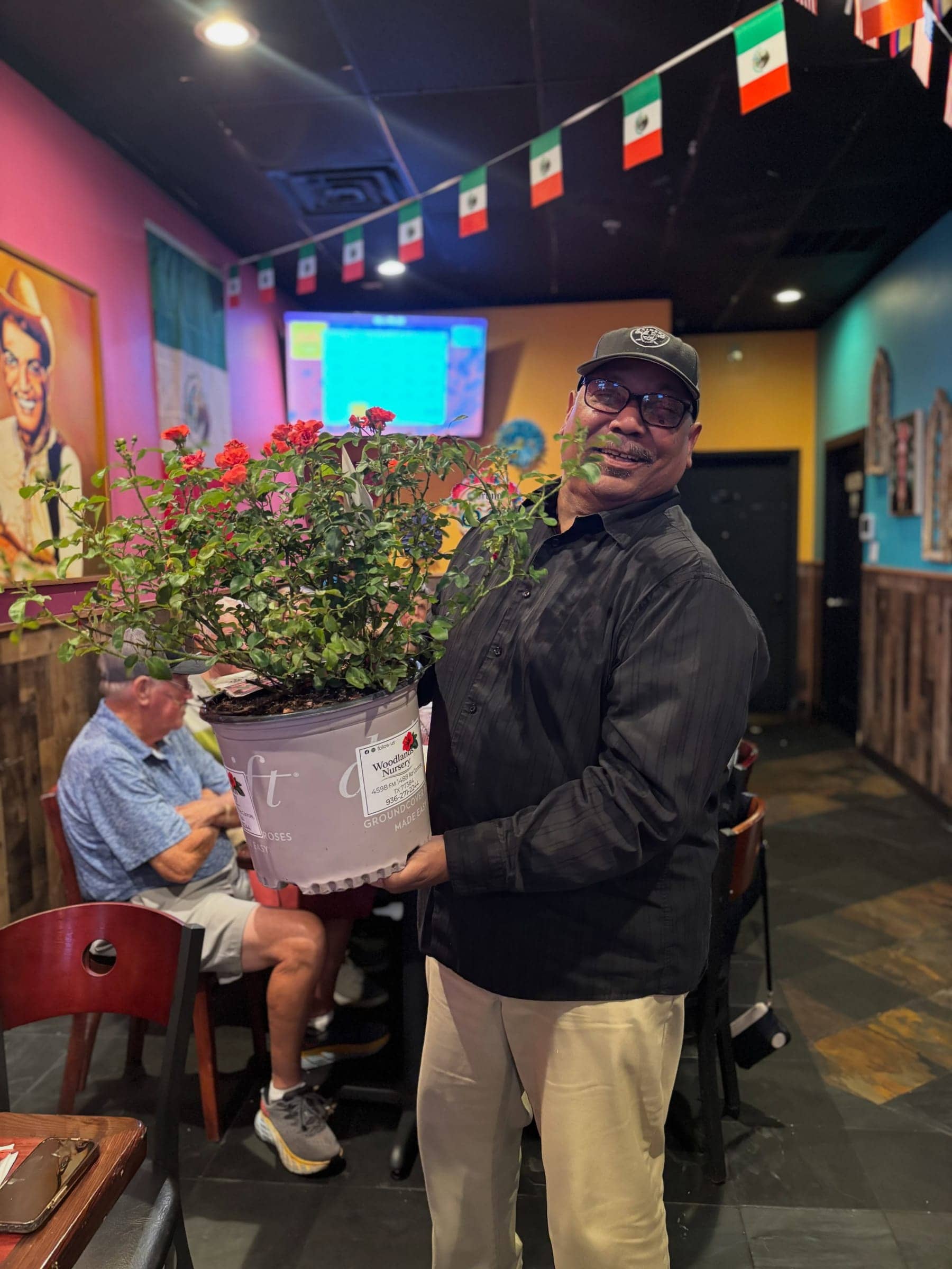 A customer holding a large pot of red flowers